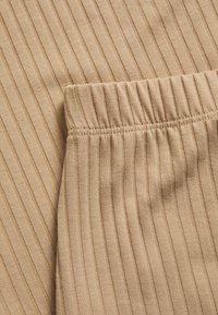 Tejido acanalado beige con una textura suave y una cinturilla elástica. El patrón presenta líneas verticales estrechas en todo el material.