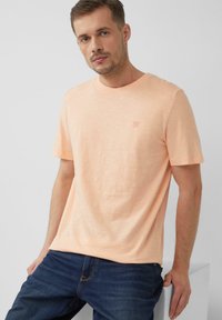 Korte mouwen, ronde hals t-shirt van zacht perzik katoen. Heeft een subtiel logo op de borst en een relaxte pasvorm. Gecombineerd met donkerblauwe jeans.