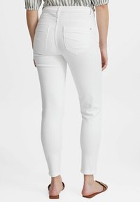 Bílé úzké džíny s vysokým pasem, zadními kapsami a hladkou texturou; zobrazené zezadu, s přiléhavým střihem.