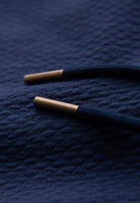 Gros plan d'un tissu texturé bleu foncé avec deux extrémités de lacets bleu foncé coiffées d'aglets en bronze.