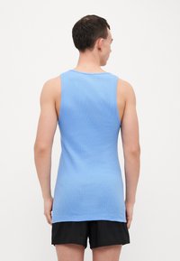Light blue, sleeveless tank top made of ribbed fabric, with a rounded neckline and a straight hem, worn with black shorts.