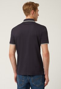 Polo shirt blu navy con colletto e polsini a righe bianche. Maniche corte e una finitura in cotone liscia. Indossato con jeans in denim blu.