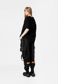 Camiseta negra de gran tamaño con letras texturizadas, combinada con pantalones cargo negros de corte relajado que presentan bolsillos y acentos naranjas. Calzado negro incluido.