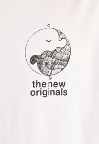 Hvidt stof med et grafisk design, der viser en yin-yang-lignende cirkel. Den ene side er glat, den anden har et tekstureret mønster. Teksten lyder "de nye originale."