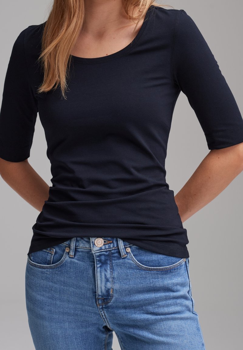 Haut bleu marine ajusté à manches trois-quarts, fabriqué en tissu doux mélange de coton, associé à un jean bleu clair légèrement délavé.