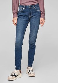 Hubené modré denimové džíny s jemným odřením, pět kapsami a hnědým stehem, doplněné béžovými a námořnickými teniskami.