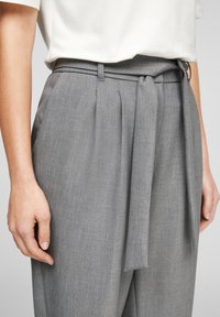 Grijze op maat gemaakte broeken hebben een gladde textuur, een hoge taille en een afneembare riem die vooraan is gestrikt. Plissé's zorgen voor een gestructureerde uitstraling.
