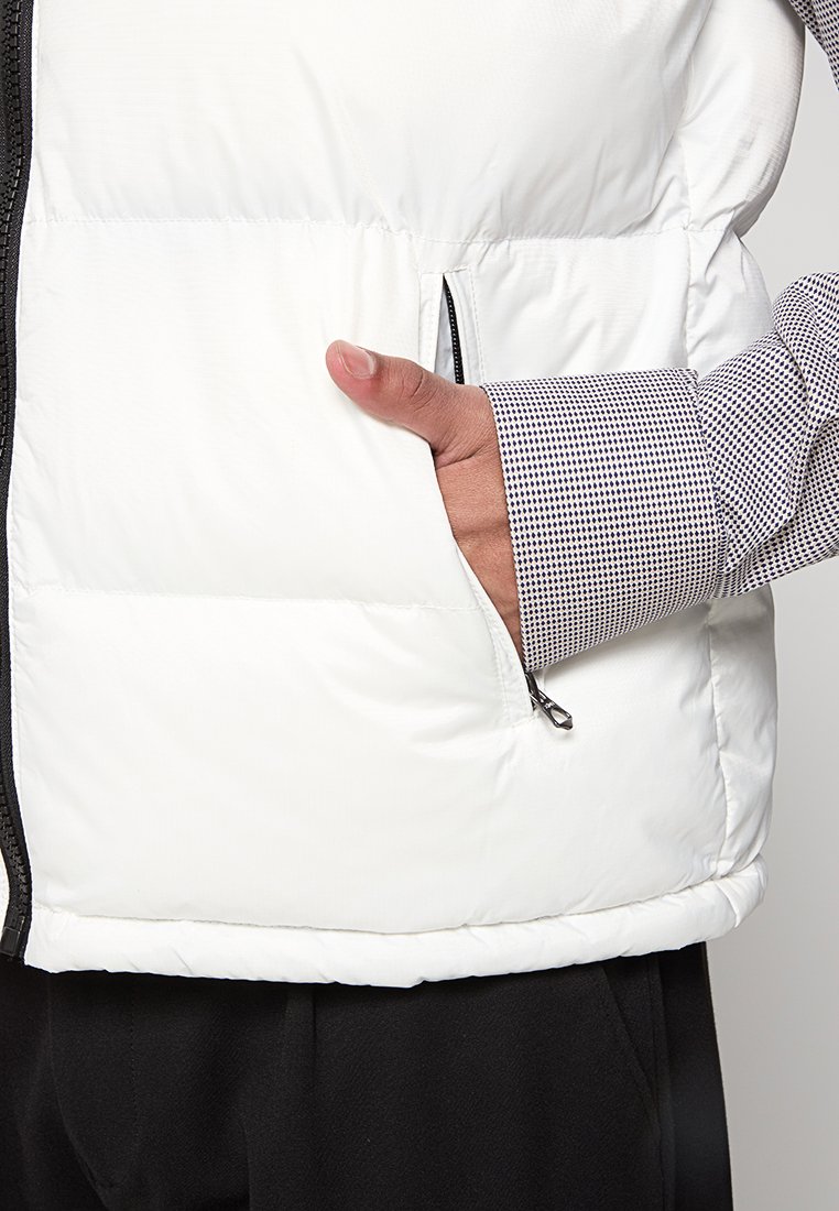 Main tenant une manche de chemise à motifs insérée dans la poche zippée d'un gilet rembourré blanc.