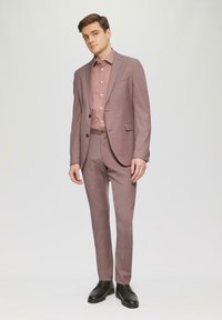 Zweiteiliges Anzug in hellmauve Stoff, mit einem einreihigen Jackett und geraden Hosen. Kombiniert mit einem passenden Hemd und schwarzen Schuhen.