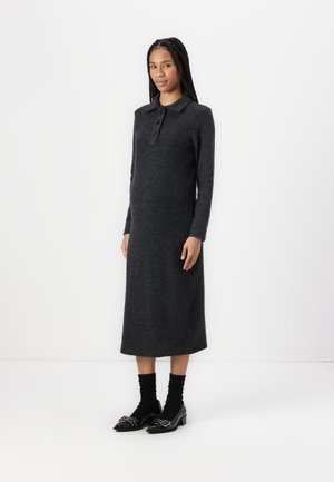 Long dark gray wool dress with a polo collar, button closure, and side slits. Worn with black ankle socks and block-heeled shoes with embellishments.