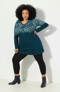 Tiffanysin värinen tunika, jossa on valkoista kukkakirjontaa vartalon alueella, yhdistettynä mustiin legginsseihin ja nilkkasaappaisiin. Pehmeä, tekstuuriainen kangas.