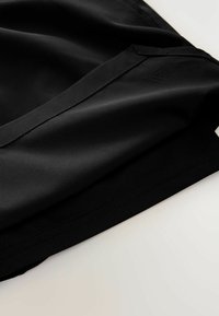 Schwarzer Sportstoff mit glatter Textur, ausgestattet mit einem gefalteten Saum und einem dezenten Logo-Detail. Minimalistisches Design mit klaren Linien.