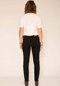 Jean noir ajusté, taille haute avec poches arrière, associé à un t-shirt blanc uni. Accessoires comprenant des bracelets en argent.