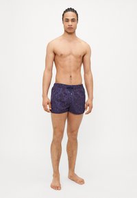 Shorts de bain de couleur violet foncé avec un motif tourbillonnant, taille élastique et cordon de serrage. Faits d'un tissu léger et à séchage rapide.