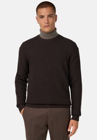 Pull en laine marron foncé avec une texture côtelée, doté d'un col haut et de manches longues, associé à un pantalon marron.