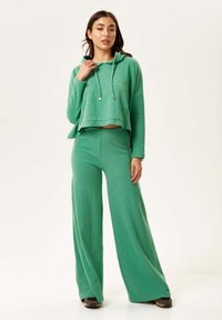 Green matching set featuring a cropped hoodie with a front pocket and drawstrings, paired with wide-leg pants. Soft fabric texture.