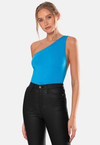 En axelbandslös blå bodysuit i stretchig tyg, kombinerad med högmidjade svarta jeans med knappstängning och fickor.