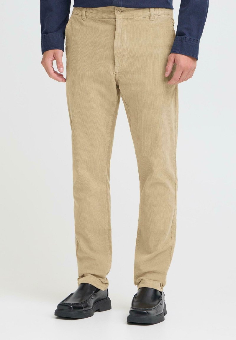 Beige kordfløyelsbukser med rett passform og frontlommer, med teksturert stoff og knappeåpning. Kombinert med svarte sko.