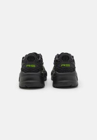 Mustat urheilukengät, joissa on verkkomateriaali yläpinta, pehmustettu kaulus, vihreät yksityiskohdat kannassa ja brändissä sekä suuri, teksturoitu pohja.