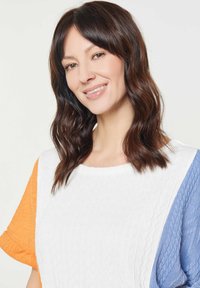 Striktrøje med en hvid krop og orange- og blå teksturerede ærmer, rund halsudskæring og intrikate kabelmønstre på ærmerne.