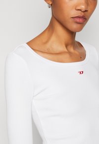 Vit långärmad skjorta med rundad halsringning och texturerad ribbad tyg. Liten röd logotyp på bröstet.