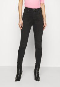 Svarta högmidjade skinny jeans med en slät yta, femficksdesign och sömmar, kombinerat med spetiga svarta klackstövlar.