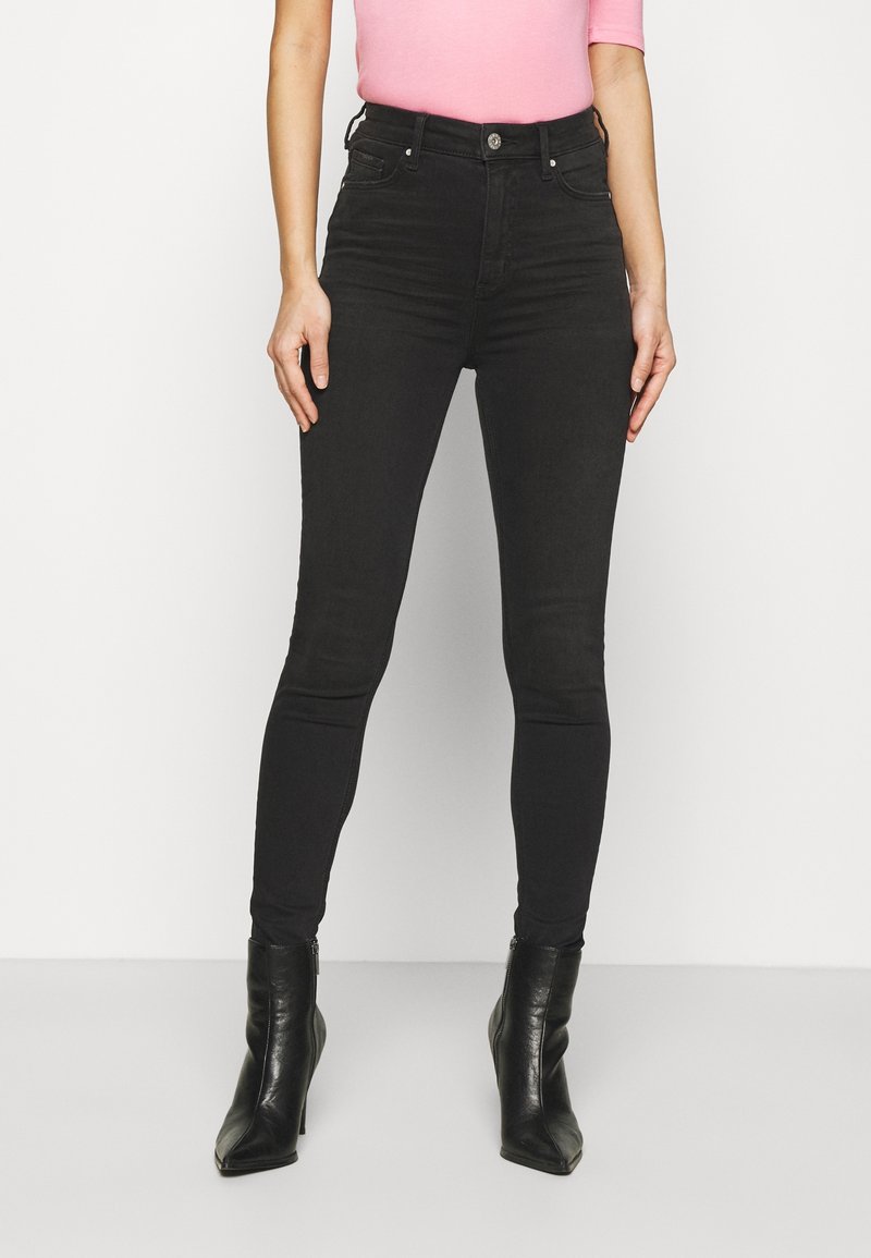 Svarta högmidjade skinny jeans med en slät yta, femficksdesign och sömmar, kombinerat med spetiga svarta klackstövlar.