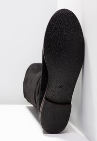 Stivale alla caviglia in suede nero con suola in gomma testurizzata. Taglia "37" visibile impressa sulla suola, che mostra una forma piatta e leggermente arrotondata.
