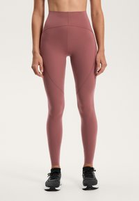 Magas derekú leggings, poros rózsaszín színben, rugalmas anyagból, sima felülettel. Díszítő varrással és rugalmas derékpánttal rendelkezik.