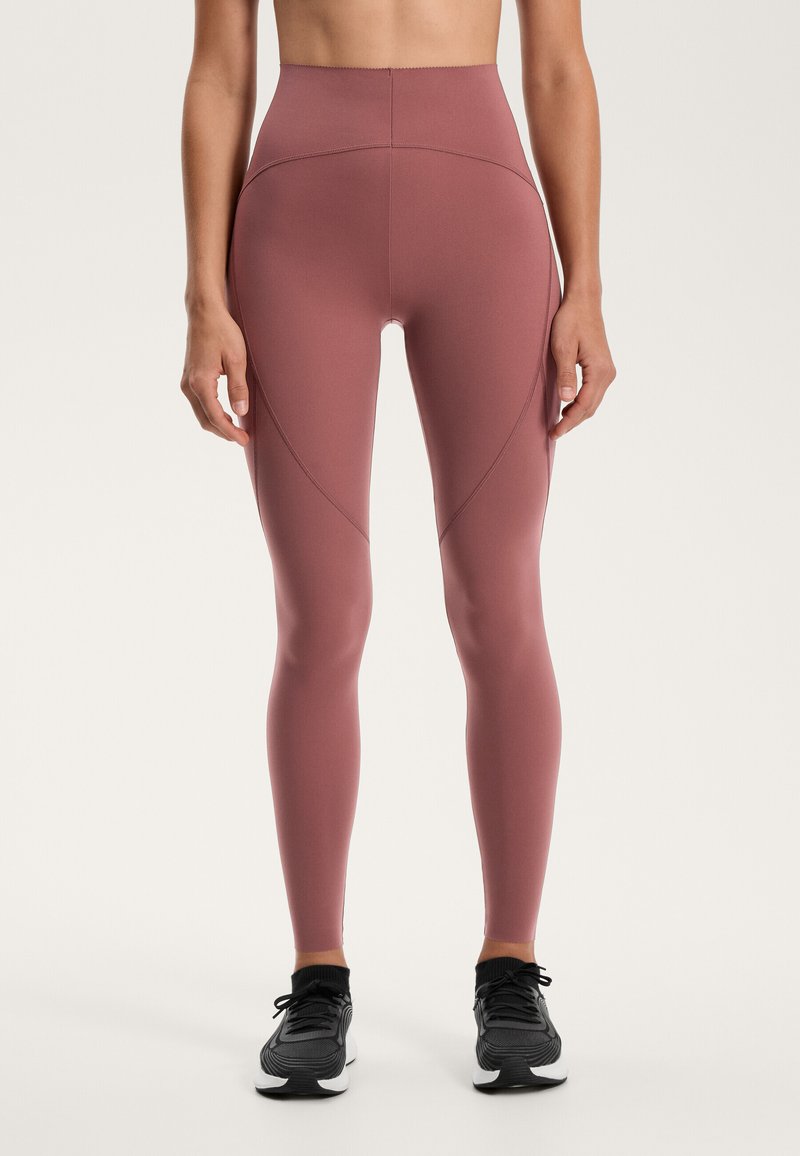 Magas derekú leggings, poros rózsaszín színben, rugalmas anyagból, sima felülettel. Díszítő varrással és rugalmas derékpánttal rendelkezik.
