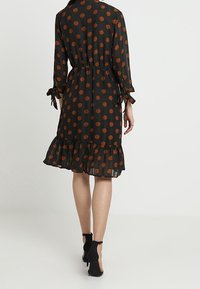 Černé šaty s velkými oranžovými puntíky, volánkovým spodním lemováním a zavazovacími rukávy, s volným střihem a stáhnutým pasem pro lepší definici.