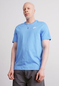 Svetlo modra bombažna majica s kratkimi rokavi in okroglim izrezom, z belim logotipom Nike na zgornji levi strani prsnega dela.