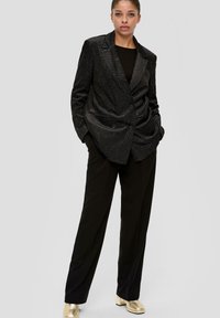 Zwarte pailletten dubbele blazer met scherpe revers, gecombineerd met losse zwarte broek en gouden blokhak schoenen. Gladde textuur.