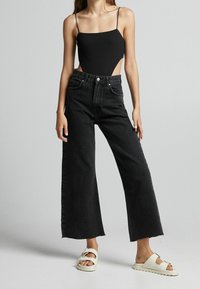 Svarta vida jeans med hög midja, fransig nederkant, kompletterade med en åtsittande svart bodysuit och vita plattformssandaler.