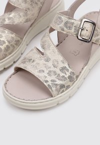 Sandalias metálicas doradas con estampado de leopardo, que cuentan con dos tiras anchas cruzadas y una hebilla, montadas sobre una suela de goma blanca.