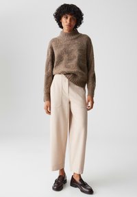 Maglione marrone con texture e collo alto abbinato a pantaloni a gamba larga color crema e mocassini scuri. Palette di colori neutri con forme distinte.