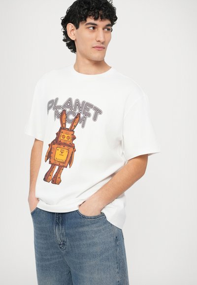 Λευκό μπλουζάκι κοντομάνικο με γραφικό ενός ρομπότ με πορτοκαλί και κίτρινες πινελιές, με την επιγραφή «PLANET NCM», συνδυασμένο με μπλε τζιν.