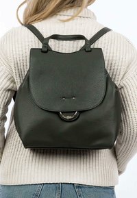 Mochila de cuero verde oscuro con forma redondeada, cierre de solapa, acentos de metal y correas ajustables. Superficie texturizada visible.