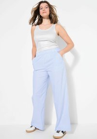 Pantalons larges rayés bleu clair avec une taille élastique et des poches latérales, associés à un débardeur argenté ajusté et des chaussures décontractées.