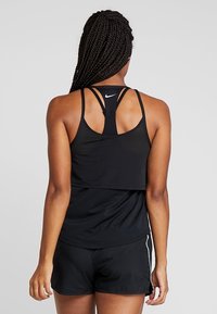 Sort atletisk tanktop med ribbet tekstur, racerback-design og et lille hvidt Nike-logo. Parret med sorte shorts med hvide accenter.