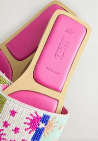 Sandales avec des motifs de soleil et d'étoile multicolores en perles sur les brides et des semelles rembourrées roses marquées « Next » et « Wide Fit » dans des cadres beiges.