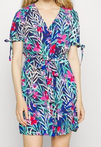 Abito a fantasia floreale con sfondo blu navy, maniche corte, dettagli legati e vita cintrata. Tessuto leggero con una vestibilità morbida.