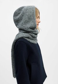 Grijze wollen sjaal met een oversized capuchon, gekenmerkt door een zachte, gestructureerde afwerking en een lusvormige wikkeling, gecombineerd met een donkere jas.