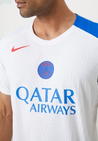 Hvid Nike sportsjersey med blå accenter. Har struktureret stof, rød logo og tekst som lyder "QATAR AIRWAYS." Klassisk crew neck design.