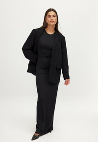 Juodas prigludęs suknelė su raukiniais, derinama su per dideliu juodu bleizeriu. Tinkamo fasono siluetas, lygus tekstūras ir smaili juoda avalynė.