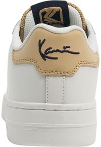 Zapatillas para hombre con parte superior de cuero blanco, acento en el talón en beige, firma en la parte trasera y suela blanca texturizada.