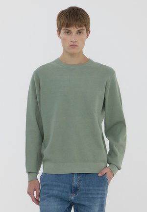 Felpa a maniche lunghe verde chiaro a coste con scollatura rotonda, texture morbida e vestibilità comoda, abbinata a jeans in denim blu.