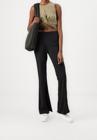 Oliwkowy, krótkie, bezrękawnik z twistem z przodu; czarne, dopasowane, rozszerzane spodnie; jasne sneakersy; szara torba.