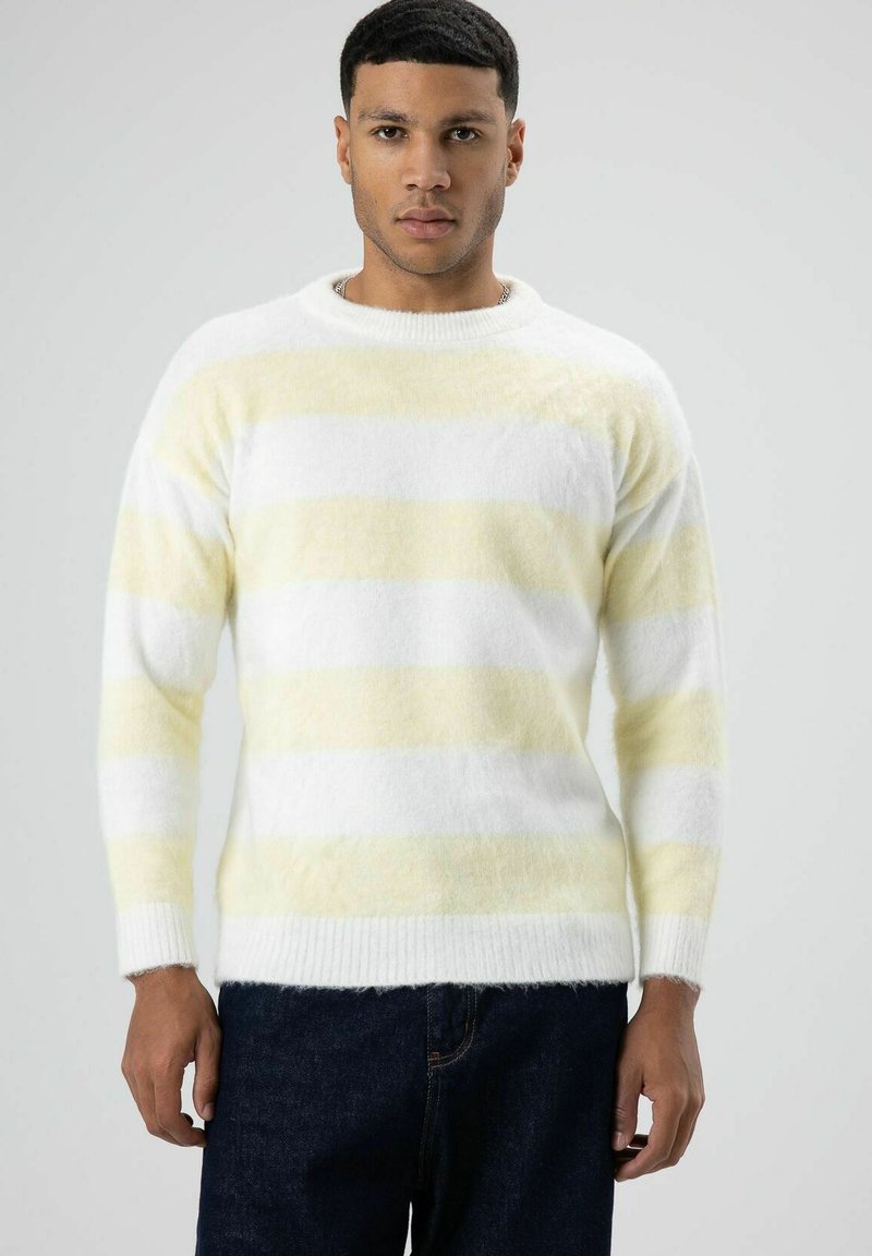 Wit en lichtgeel gestreepte trui, gemaakt van zacht materiaal met een ronde hals en geribbelde manchetten, gecombineerd met een blauwe spijkerbroek.