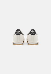 Zapatillas de cuero blancas con detalles en negro, que cuentan con una suela de goma texturizada y el icónico logo de tres rayas en el talón.